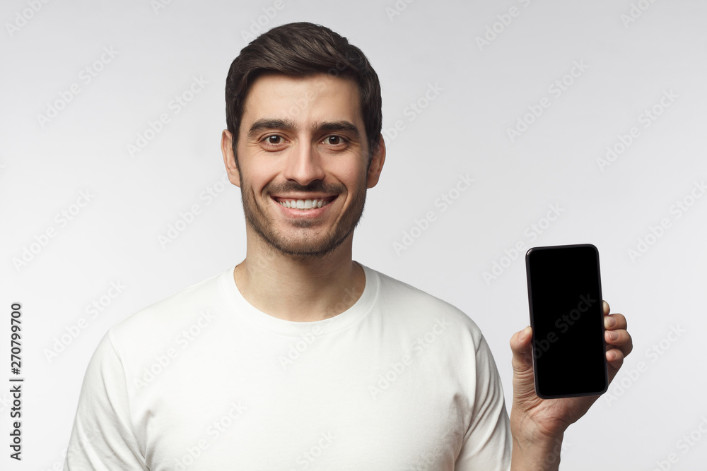 Young smiling man showing blank screen of smart phone in hand, isolated on gray background Young smiling man showing blank screen of smart phone in hand, isolated on gray background