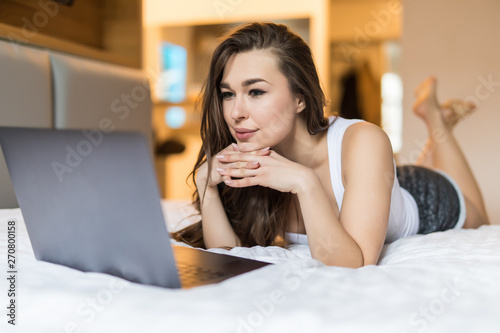 Smiling woman catching up on her social media as she relaxes in bed with a laptop on a lazy day