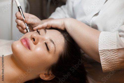 Close up side view portrait of a cute caucasian woman doing noninvasive microdermabrasion on her face with a dermapen by a cosmetician. photo