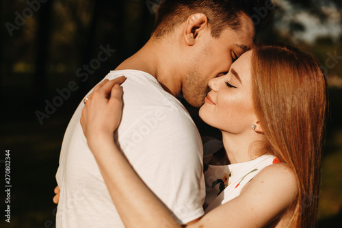 Close up portrait of a lovely caucasian female with red hair and freckles embracing her boyfriends with closed eyes outside while dating. photo