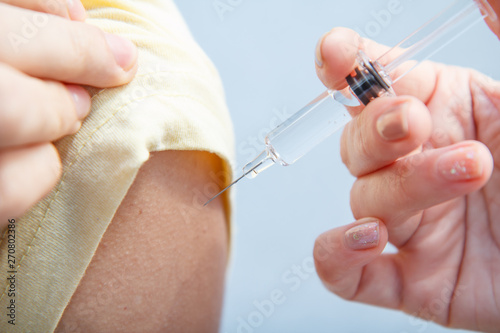 Hand of doctor holding syringe for vaccination to upper arm of patient.