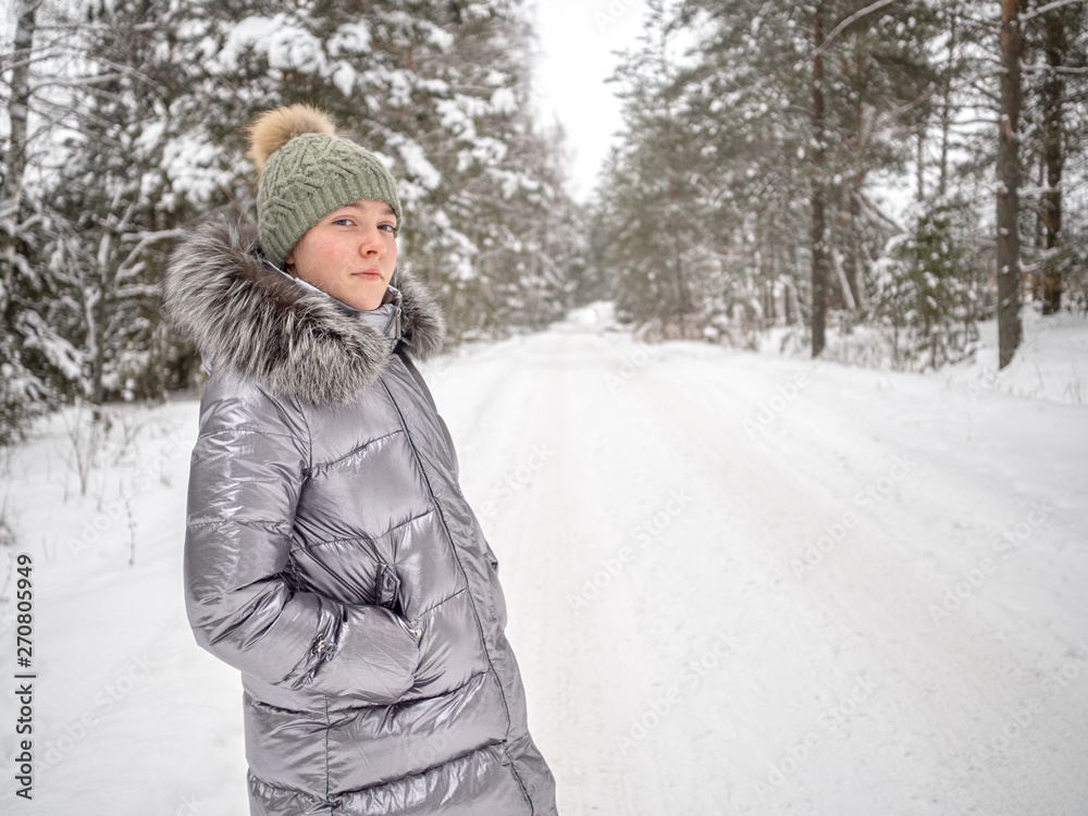 A young girl walks in the winter forest and enjoys silence. She is wearing a hat and a jacket of silver color A young girl walks in the winter forest and enjoys silence. She is wearing a hat and a jacket of silver color