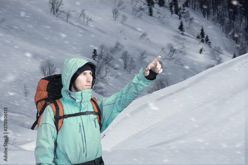 Portrait of adventurous young man on winter mountainside view pointing out. Active lifestyle and tourism.