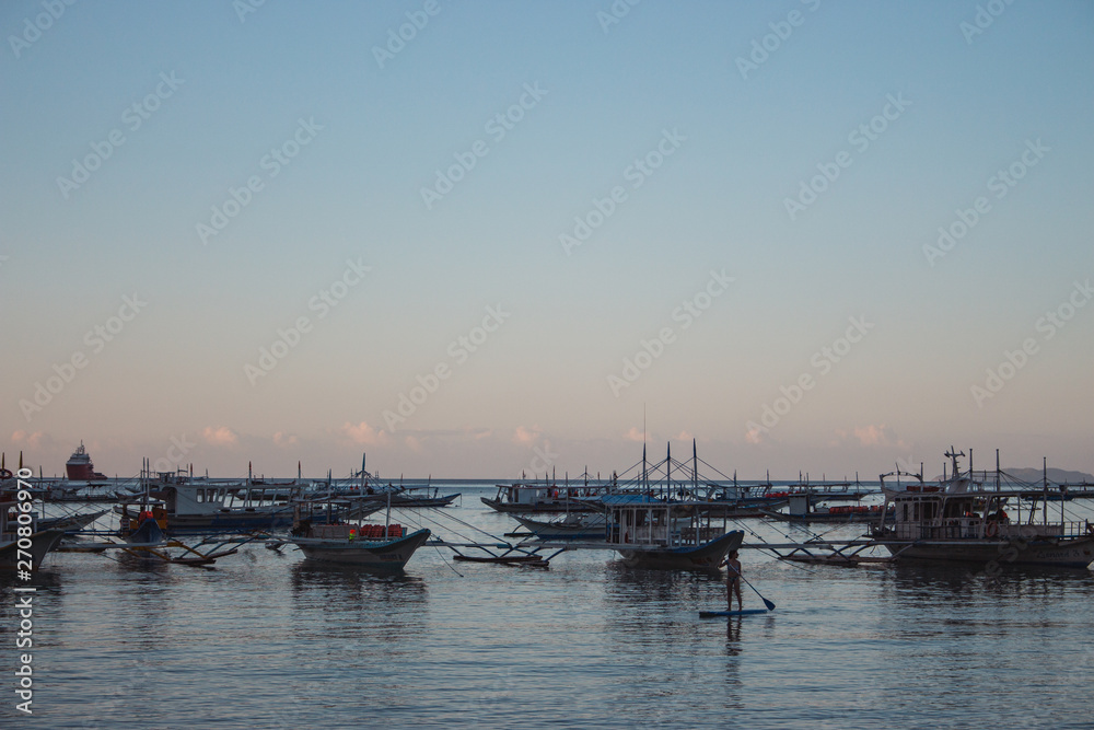 Many boats in tropical harbor in the evening. Sunset in lagoon in Philippines,Palawan, El Nido. Traditional philippines sailboats. Summer vacation and travel. Boats silhouettes in evening sea. 