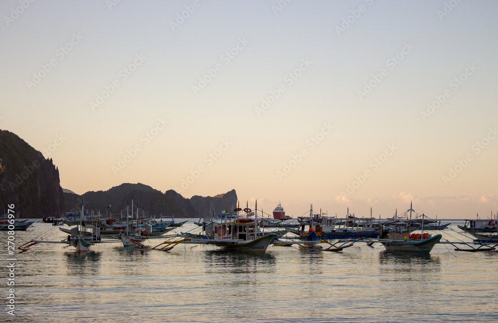 Many boats in tropical harbor in the evening. Sunset in lagoon in Philippines,Palawan, El Nido. Traditional philippines sailboats. Summer vacation and travel. Boats silhouettes in evening sea. 