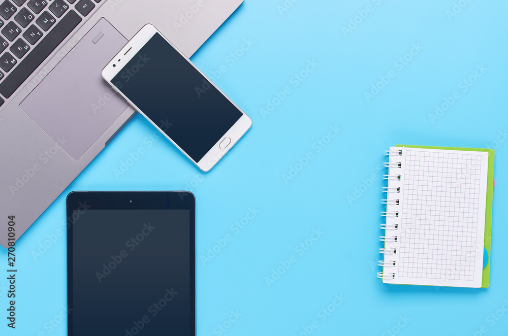 top view upon gadgets on blue background, the composition of a laptop, white headphones, phone, glass with a drink and car keys top view upon gadgets on blue background, the composition of a laptop, white headphones, phone, glass with a drink and car keys
