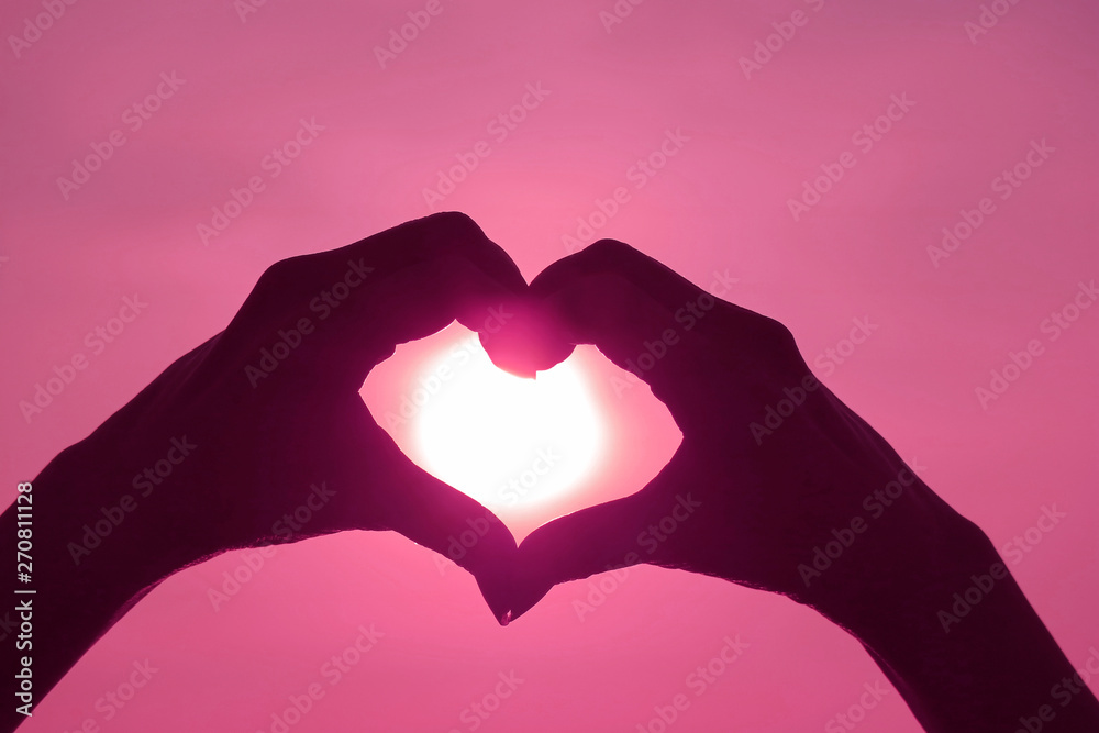 Obraz premium Pink Colored silhouette of female's hand posing LOVE HEART sign against shiny sun