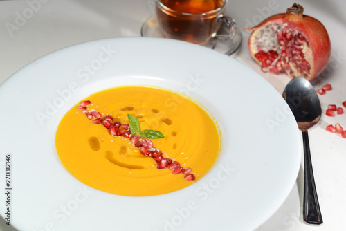pumpkin cream soup on a white plate decorated with pomegranate seeds and spices