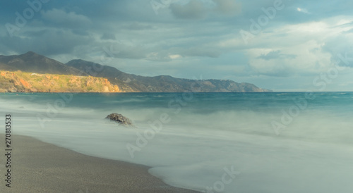 Nerja  Malaga  Spain - March 20  2019  Panoramic of a lonely beach with lighted mountains in the distance under a stormy sky