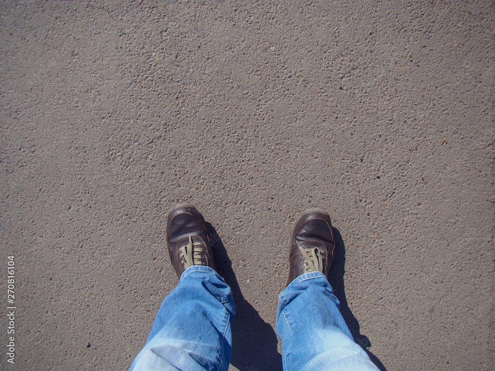 Fototapeta premium Top view on brown boots, green laces, blue jeans. Background - asphalt.