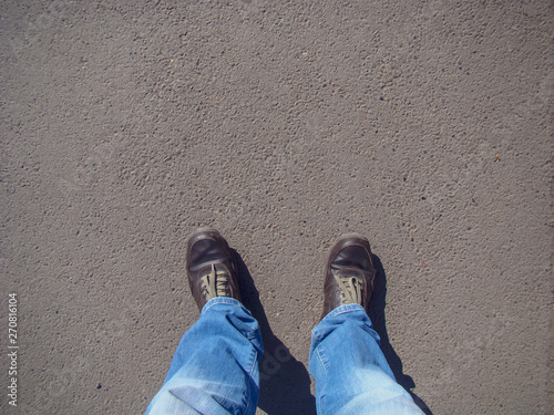 Top view on brown boots, green laces, blue jeans. Background - asphalt.