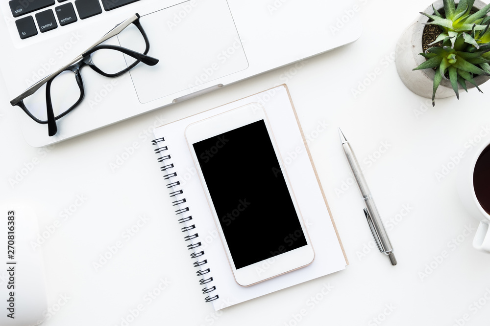 White smartphone with black blank mock up screen is on top of white office desk table with supplies. Top view with copy space, flat lay. White smartphone with black blank mock up screen is on top of white office desk table with supplies. Top view with copy space, flat lay.