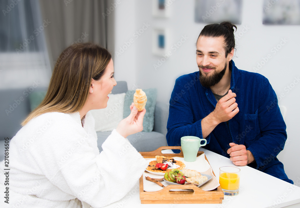 beautiful young couple having breakfast in bath robe, blond attractive size plus female model and bearded male model