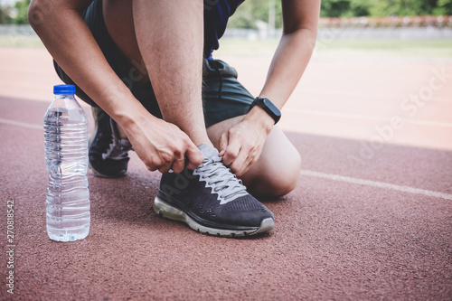Young fitness athlete man running on road track, exercise workout wellness and runner tying shoelaces with copy space before run
