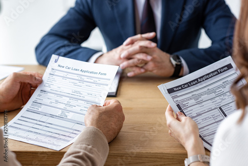 cropped view of customers holding contracts near car dealer with clenched hands