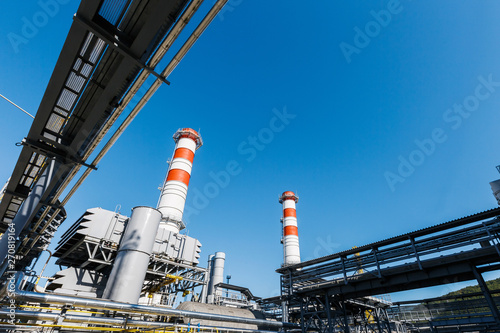 Gas turbine power plant on natural gas with chimneys of red-white color against a blue sky on a sunny day