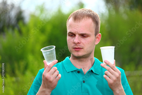 A man in a Marrs green T-shirt demonstrates a plastic disposable cup and an environmentally friendly paper cup. photo