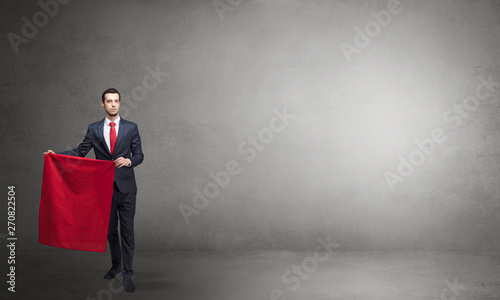 Businessman standing with red toreador cloth in his hand in an empty room  