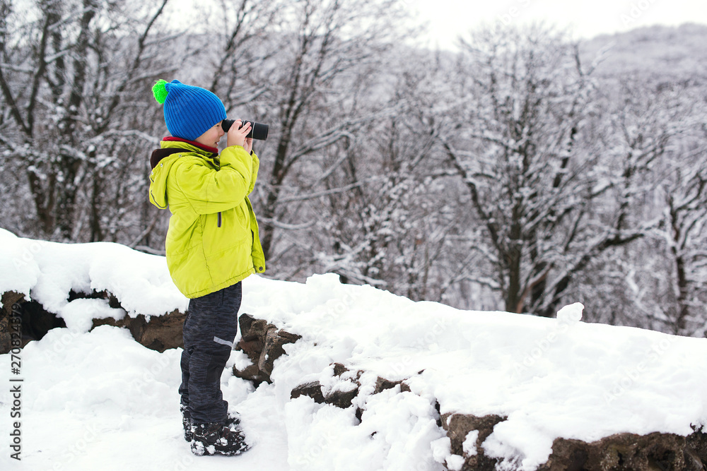 Сute kid nature explorer in winter forest. Little boy binoculars explorer at winter nature. Winter vacation.