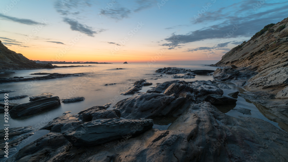 A long exposure of a colored sunrise above the seashore rocks and cliffs. 