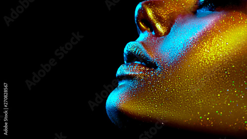 Fashion model woman skin face in bright sparkles, colorful neon lights, beautiful sexy girl lips, mouth. Trendy glowing gold skin make-up. Art design make up. Glitter metallic shine makeup © Subbotina Anna