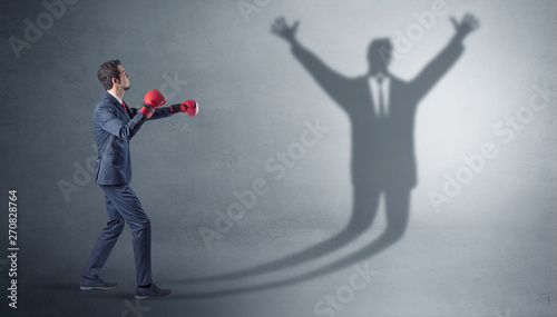 Businessman with boxing gloves fighting with disarmed businessman shadow 