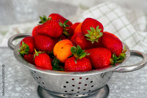 Strawberries and apricots in a colander on the table.