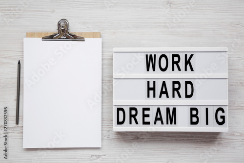 Lightbox with 'Work hard dream big' words, clipboard with blank sheet of paper on a white wooden surface, top view. Flat lay, overhead. photo