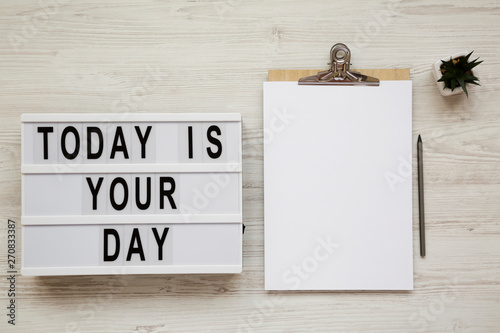 'Today is your day' on a modern board, clipboard with blank sheet of paper on a white wooden background, top view. Overhead. photo