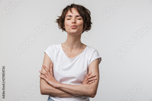 Image of beautiful woman in basic t-shirt looking at camera while standing with arms crossed