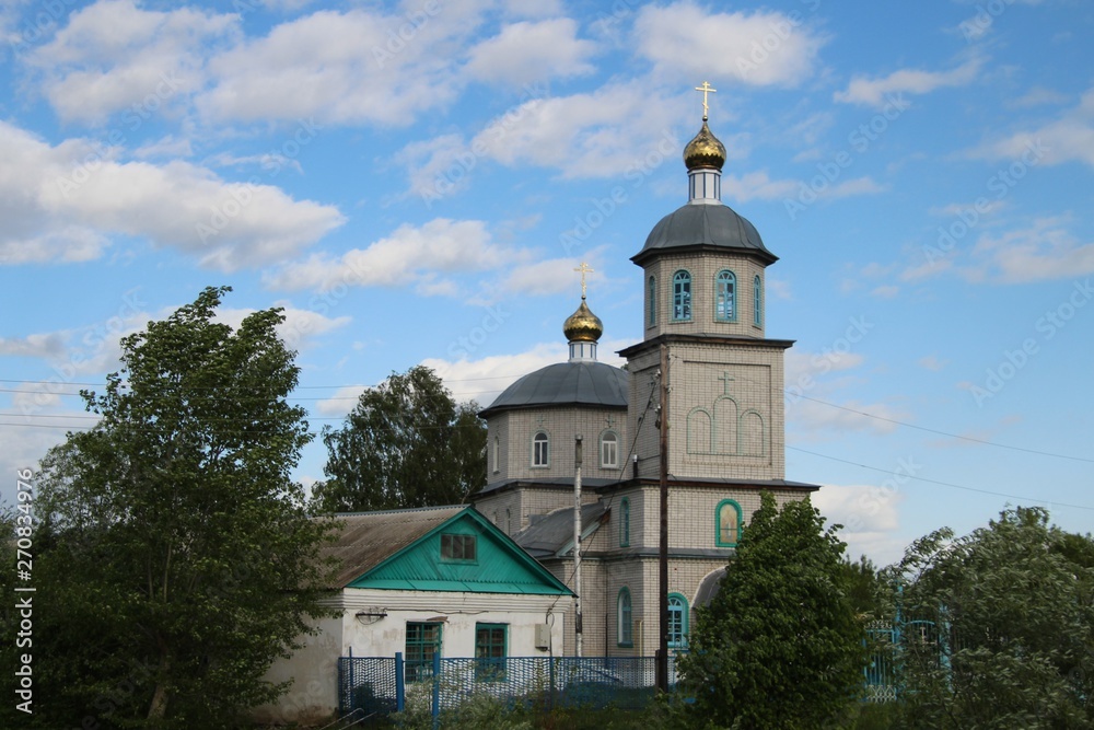 Spring landscape with a rural church under a blue sky with white clouds in the village of Ukhmany