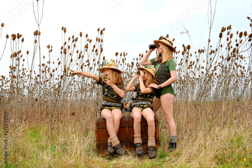 Twin young sisters and an adult girl dress up as explorers. They pose in the outdoors dressed with jungle hats and khaki safari clothes.