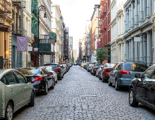 Cobblestone covered Greene Street is crowded with buildings and cars in the SoHo neighborhood of Manhattan in New York City