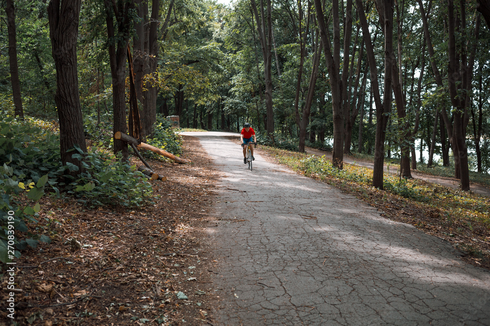A cyclist rides on a road bicycle on road in woods. A cyclist rides on a road bicycle on road in woods.