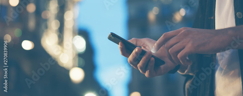 Closeup image of male hands with smartphone at night on city street, searching internet or social networks, hipster man typing an sms message on chat