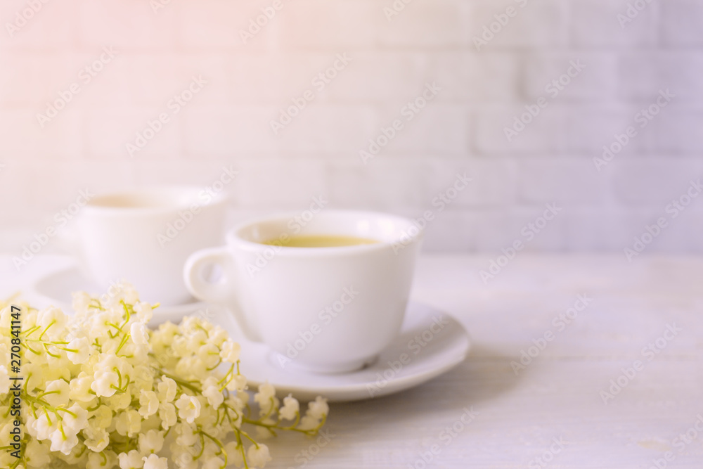morning tea in white cups and a bouquet of lilies of the valley. cups of tea and flowers. delicate background with cups of tea and lilies of the valley. morning tea in white cups and a bouquet of lilies of the valley. cups of tea and flowers. delicate background with cups of tea and lilies of the valley.