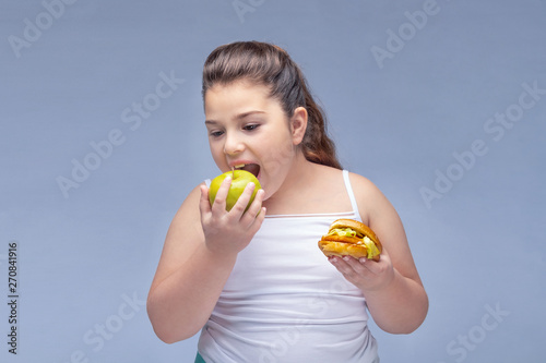 Portrait of a young beautiful girl holding a red Apple in one hand and a hamburger in the other on a white background .A true expression of positive emotions. the problem of childhood obesity