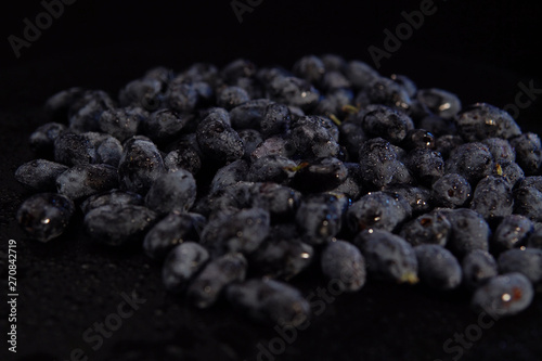 Ripe honeysuckle berries with droplets of water on against black backdrop, place for text. Dark blue berry background.Concept of healthy and proper nutrition.