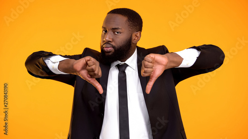 Deeply dissatisfied black man showing double thumbs-down, poor quality service photo