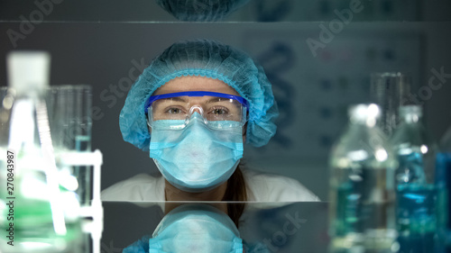 Laboratory worker in protective eyeglasses and uniform looking at camera
