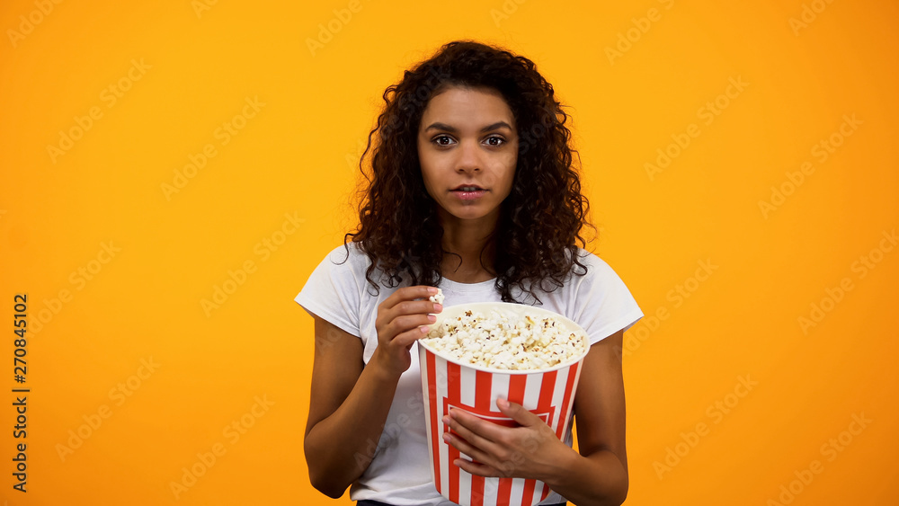 Beautiful African-American woman eating popcorn isolated on yellow background