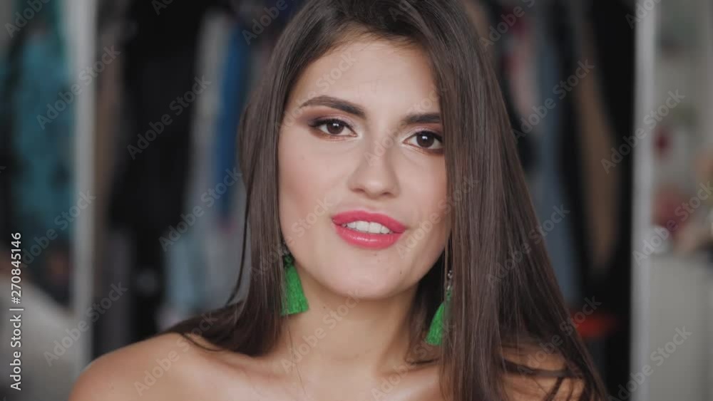 Closeup portrait of young beautiful brunette woman with bare shoulders, gorgeous eyes adorable smile, trendy makeup and brush earrings having fun in her room indoors smiling, flirting looking at Closeup portrait of young beautiful brunette woman with bare shoulders, gorgeous eyes adorable smile, trendy makeup and brush earrings having fun in her room indoors smiling, flirting looking at