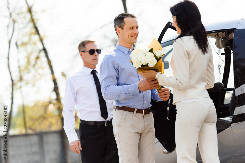 husband giving flowers to wife on romantic date near helicopter and pilot husband giving flowers to wife on romantic date near helicopter and pilot