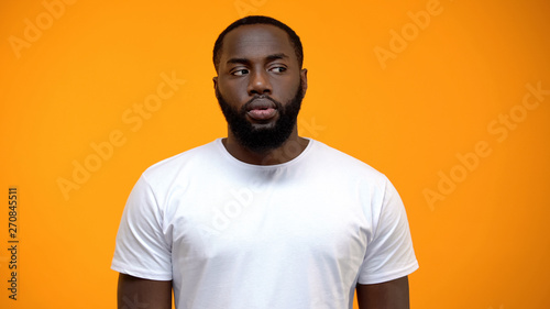 Ashamed African-American man looking to side against yellow background, guilty