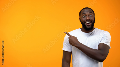 Excited black man pointing finger into background, template for text, attention
