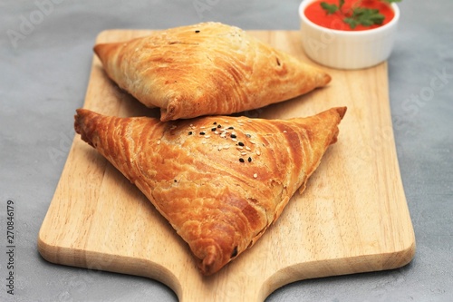 Cutting board with delicious meat samosas and red sauce on gray background
