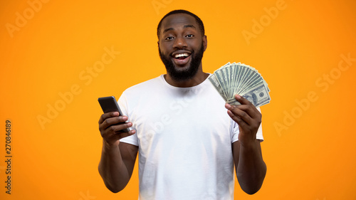 Excited Afro-American man holding smartphone and dollars, online money transfer