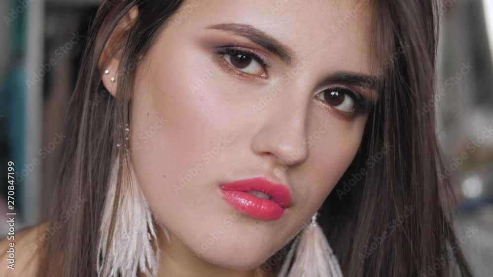 Closeup shot of young beautiful brunette woman with bare shoulders, gorgeous eyes adorable smile, trendy makeup and brush earrings having fun in her room indoors looking at camera. Makeup artist hand Closeup shot of young beautiful brunette woman with bare shoulders, gorgeous eyes adorable smile, trendy makeup and brush earrings having fun in her room indoors looking at camera. Makeup artist hand