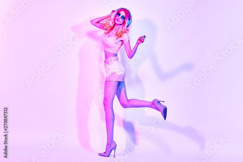 Fashion. Party fitness woman enjoy nightlife. Sexy Excited DJ girl in colorful neon light dance. Beautiful fashionable model in glamor outfit, stylish heels. Creative dancing music lover neon concept