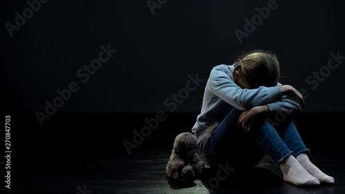 Konstfotografi Teddy bear near female child sitting alone in dark room, lack of friends